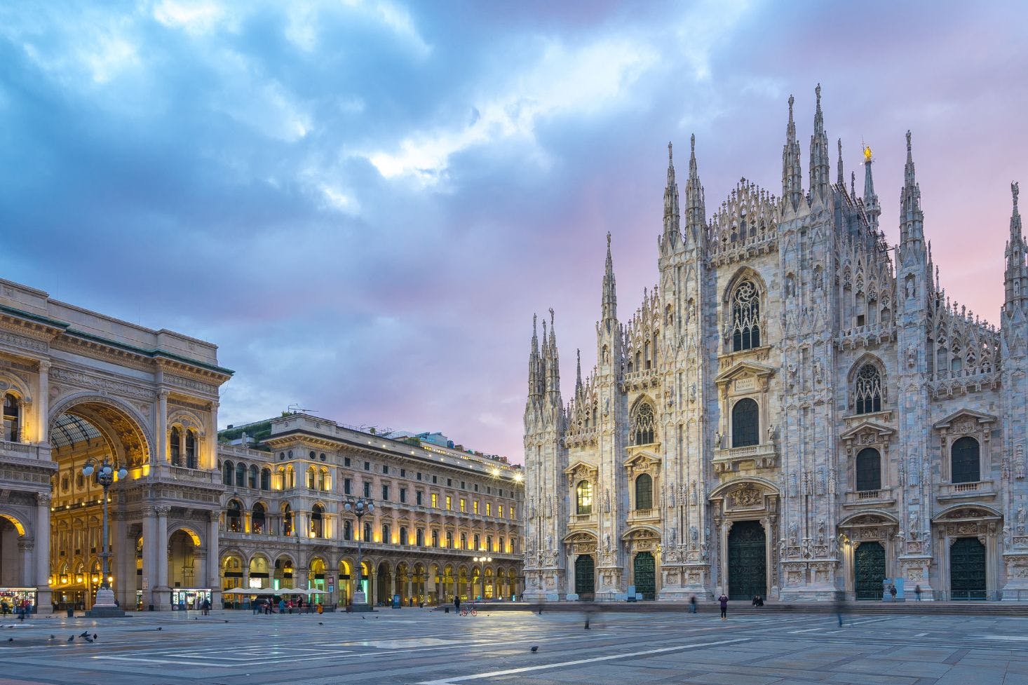 Pizza del Duomo in Milan with a sunset view of the Duomo di Milano and Galleria Vittorio Emanuele II under cloudy skies