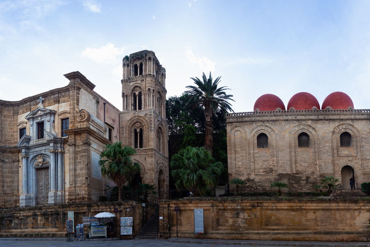 View of Chiesa Santa Maria dell'Ammiraglio and Chiesa di San Cataldo in Palermo, with palm trees and a souvenir stand with magnets and postcards in front of them