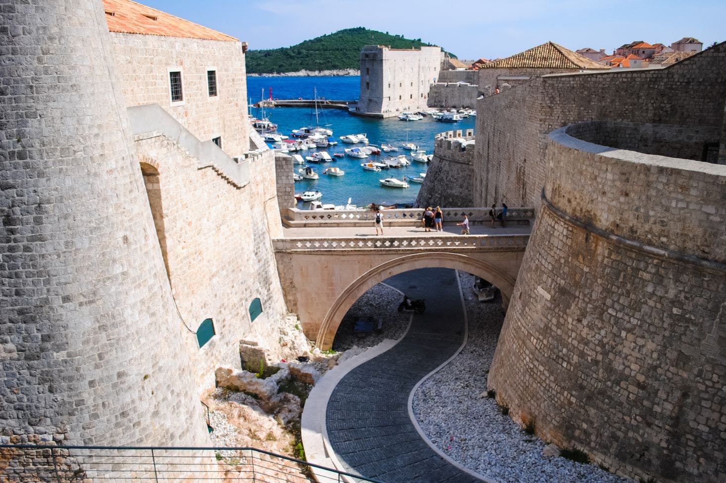 Stone walls of Dubrovnik's ancient castle with views of the city walls, harbor, and docked boat