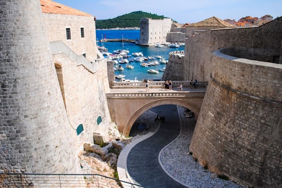 Stone walls of Dubrovnik's ancient castle with views of the city walls, harbor, and docked boat