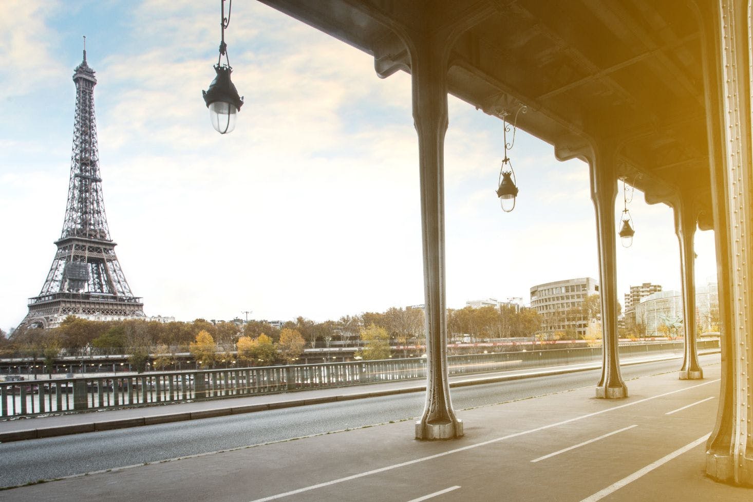 View of the Eiffel Tower through the arches of Pont de Bir-Hakeim, with trees and cityscape in the background