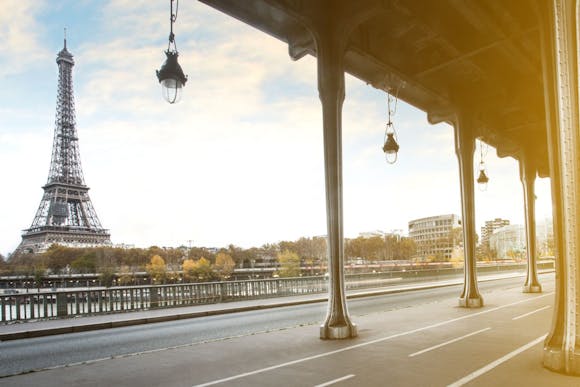 View of the Eiffel Tower through the arches of Pont de Bir-Hakeim, with trees and cityscape in the background