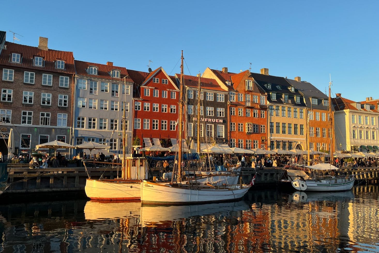 Bright and sunny Nyhavn harbor, featuring boats and colorful houses lining the waterfront