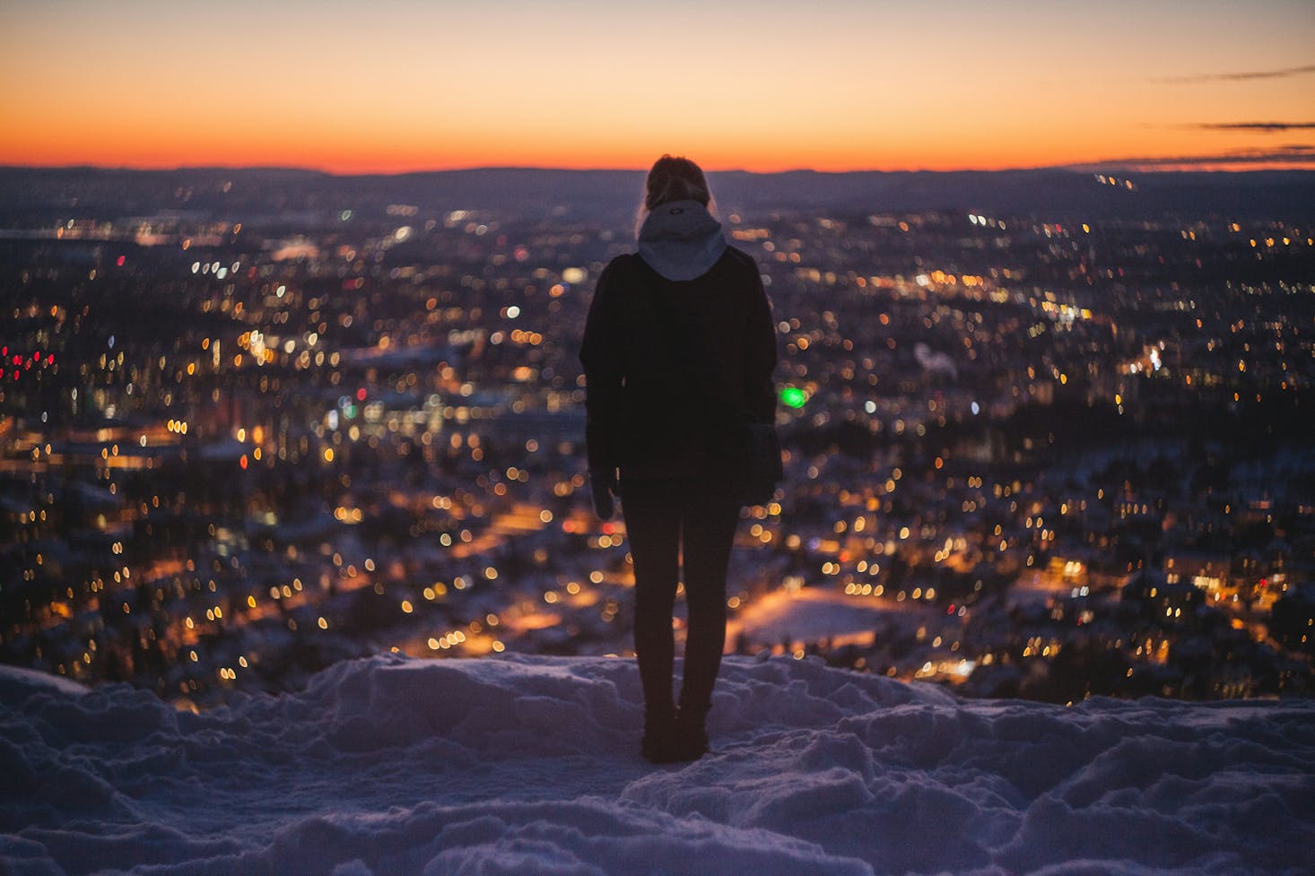 A person looking out over the city of Oslo at sunset from a snowy mountain