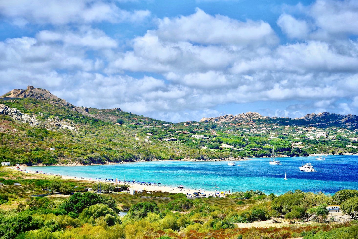 Spiaggia bianca e mare cristallino a Palau, Sardegna, con verde tutto attorno e cielo azzurro