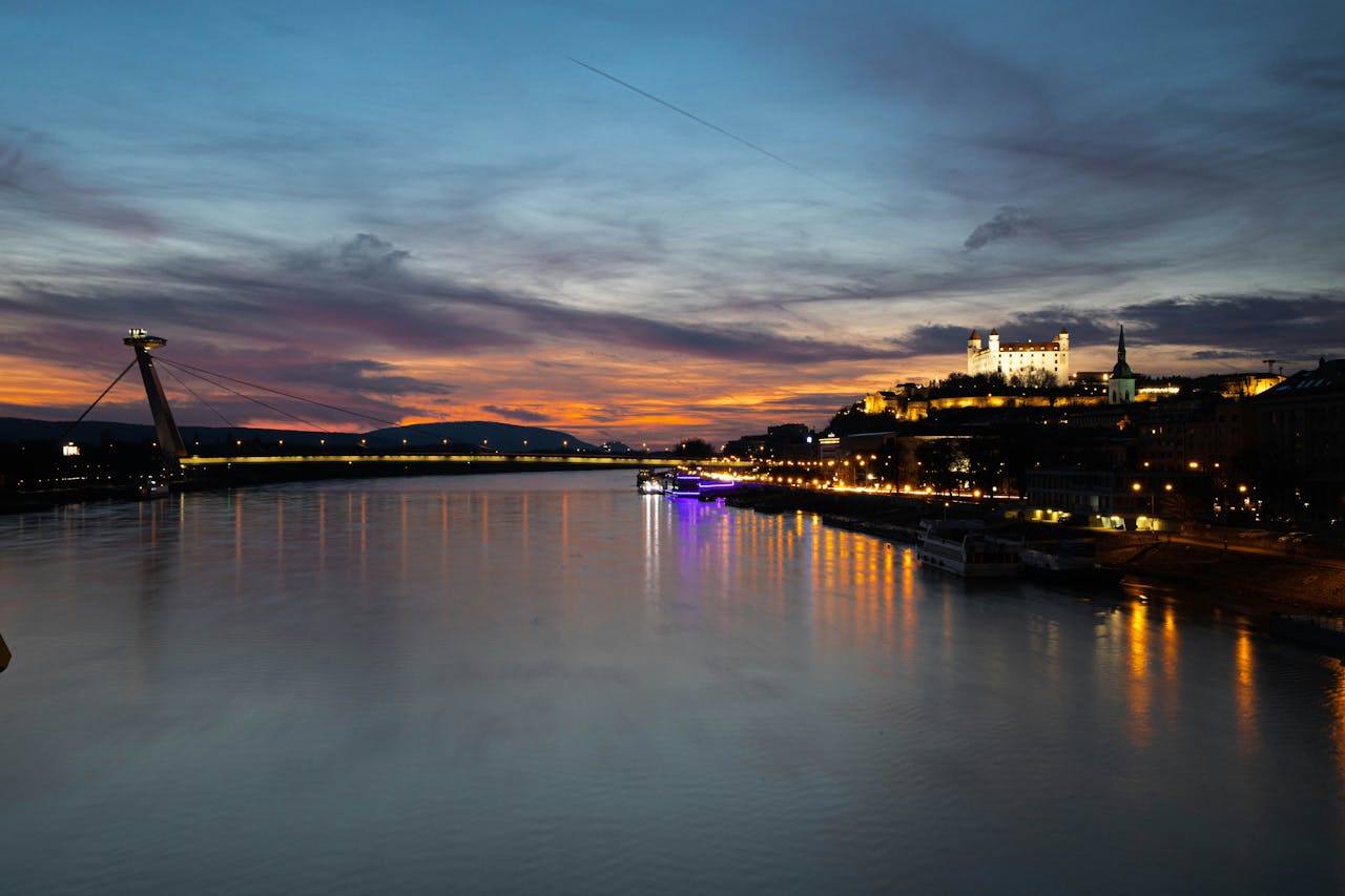 Vista dal fiume Danubio su Bratislava al tramonto, con palazzi e luci della città in lontananza 