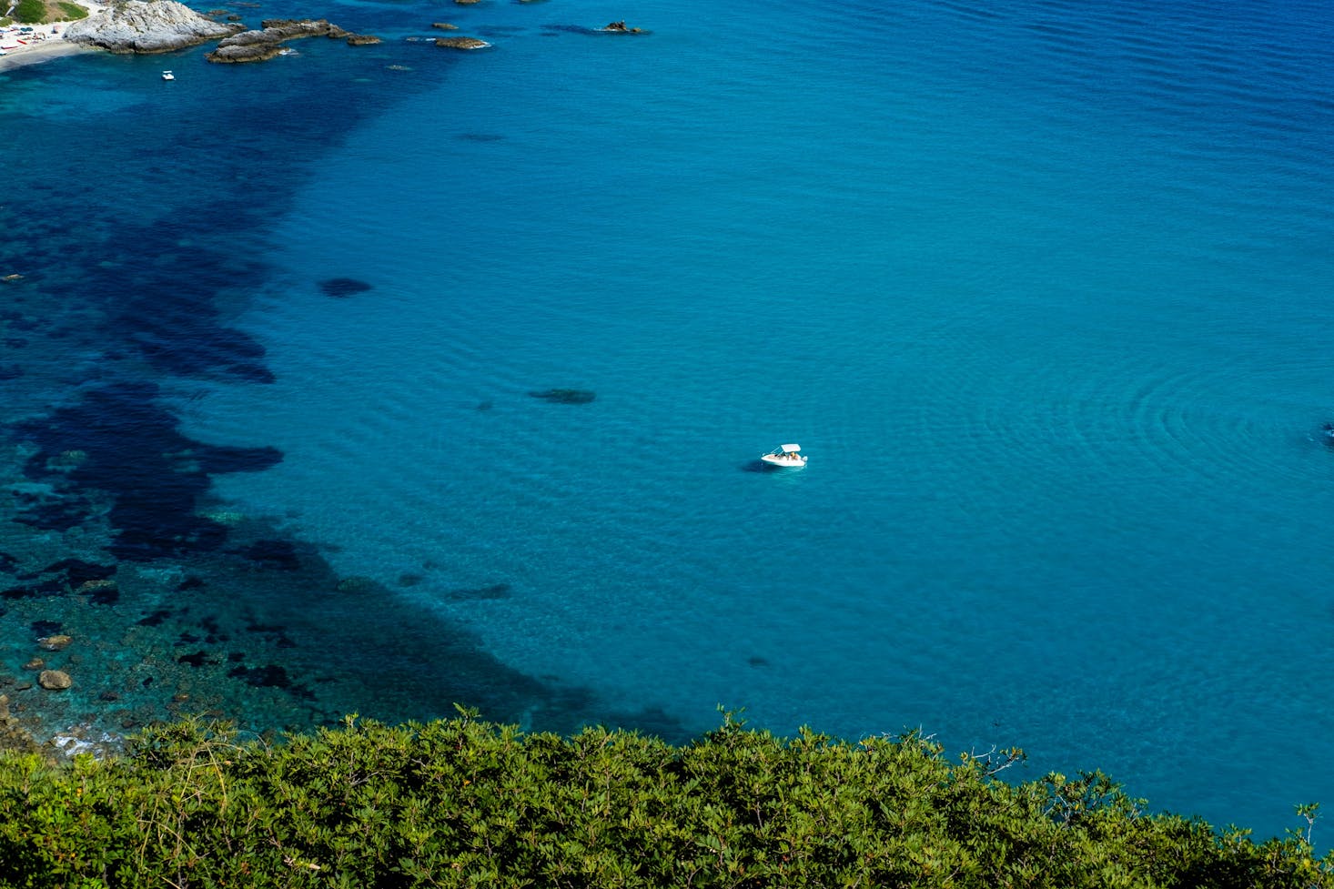 Mare blu, con del verde in primo piano e uno yacht poco distante dalla costa