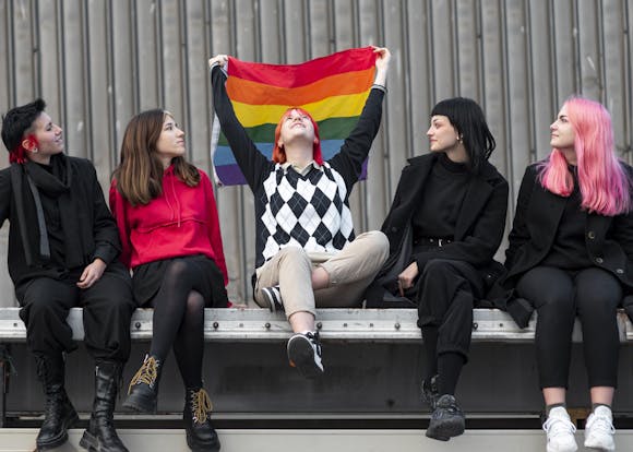 Group of individuals sitting together, with one person holding up a rainbow pride flag, celebrating inclusivity and diversity