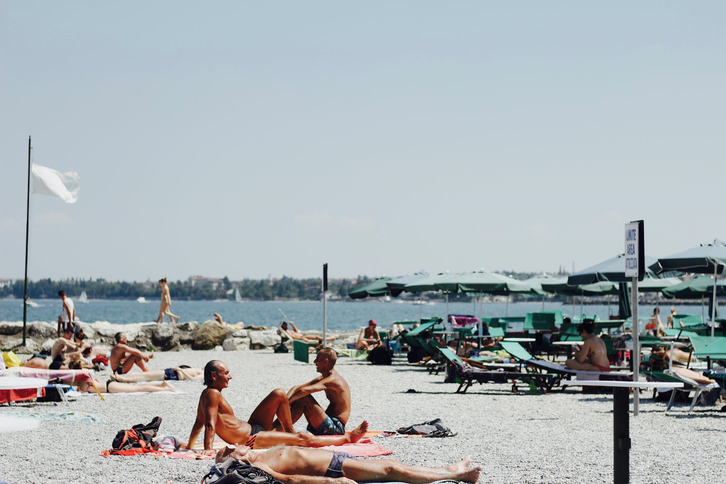 Bagnanti in spiaggia, con ombrelloni e lettini, a Desenzano del Garda, con il lago sullo sfondo