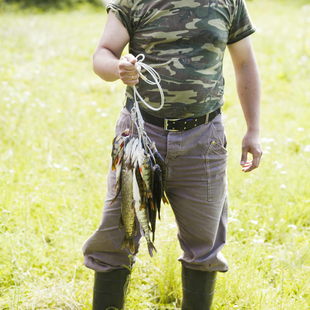 Man dressed in camouflage holding a string of freshly caught fish, showcasing outdoor skills and traditions