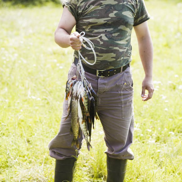 Man dressed in camouflage holding a string of freshly caught fish, showcasing outdoor skills and traditions