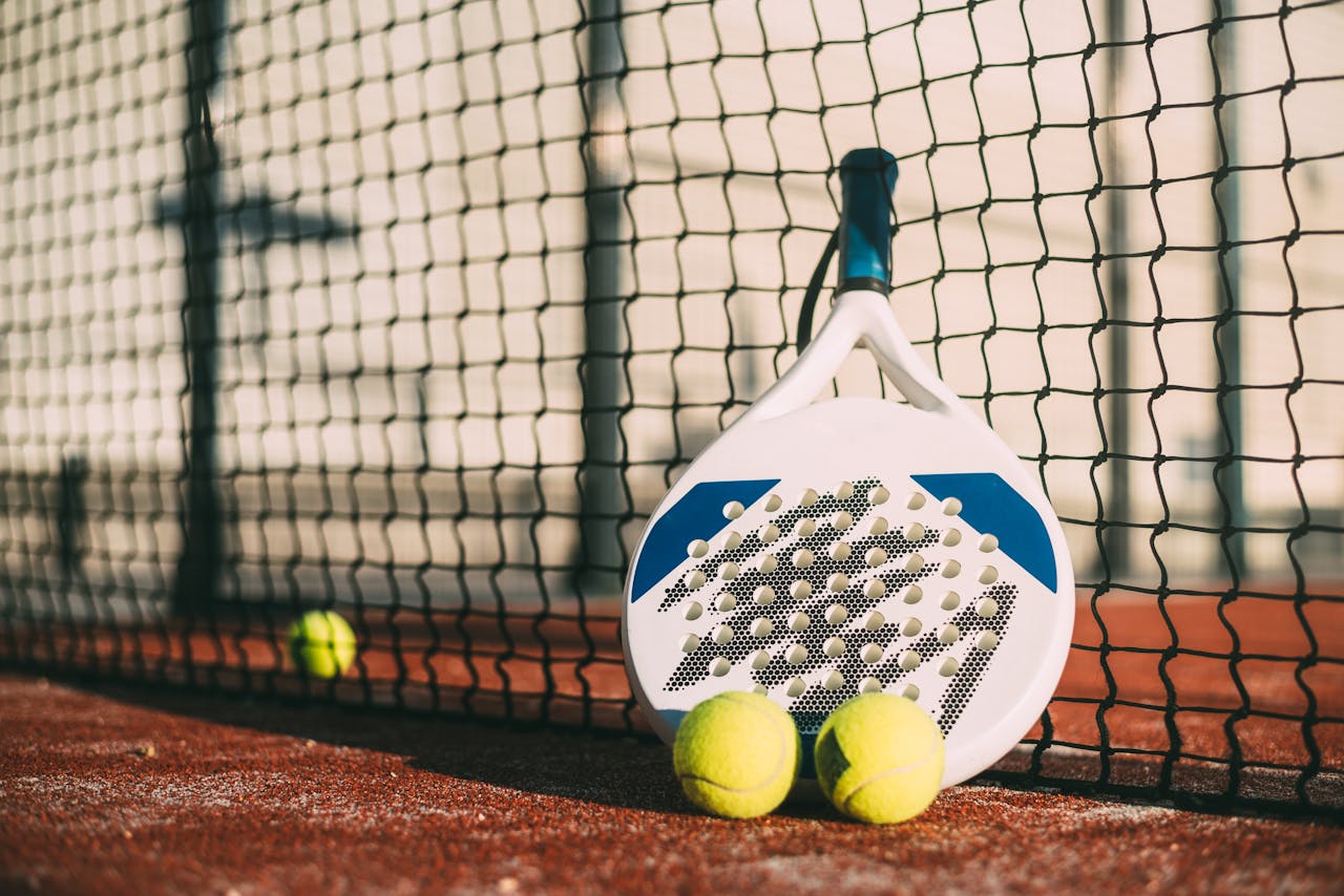 Padel racket and balls resting against a net on a clay court