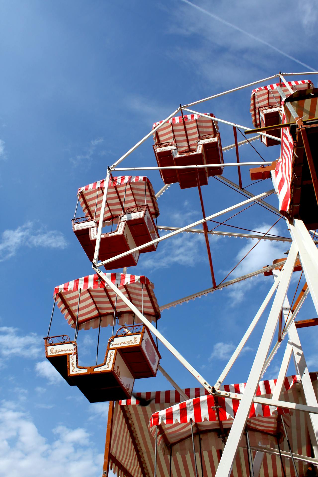 Close-up of a vintage Ferris wheel with red and white striped gondolas against a bright blue sky