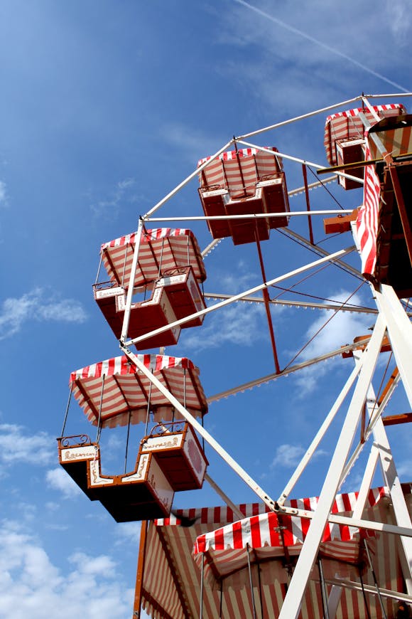 Close-up of a vintage Ferris wheel with red and white striped gondolas against a bright blue sky