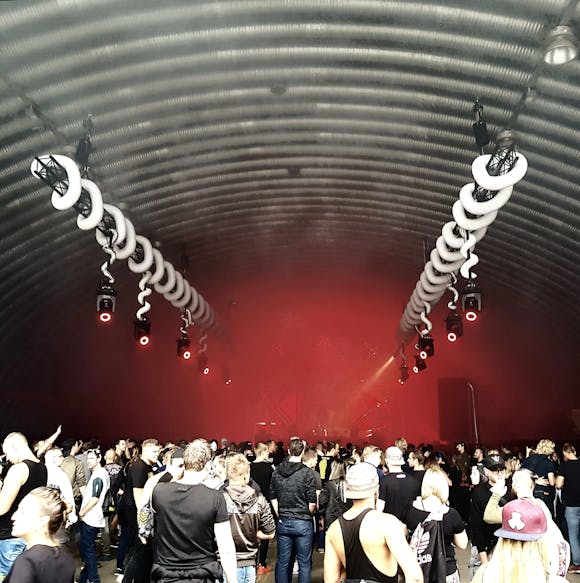 Crowd gathered inside a dimly lit venue with red lights and an industrial atmosphere, enjoying a live performance