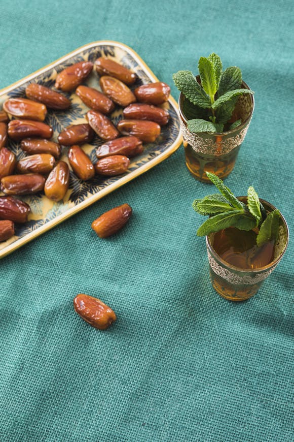 A decorative tray of fresh dates alongside glasses of mint tea on a vibrant green background