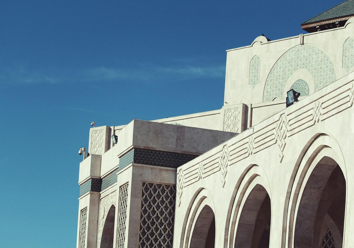 The ornate white exterior of the Hassan II Mosque in Casablanca set against the blue sky