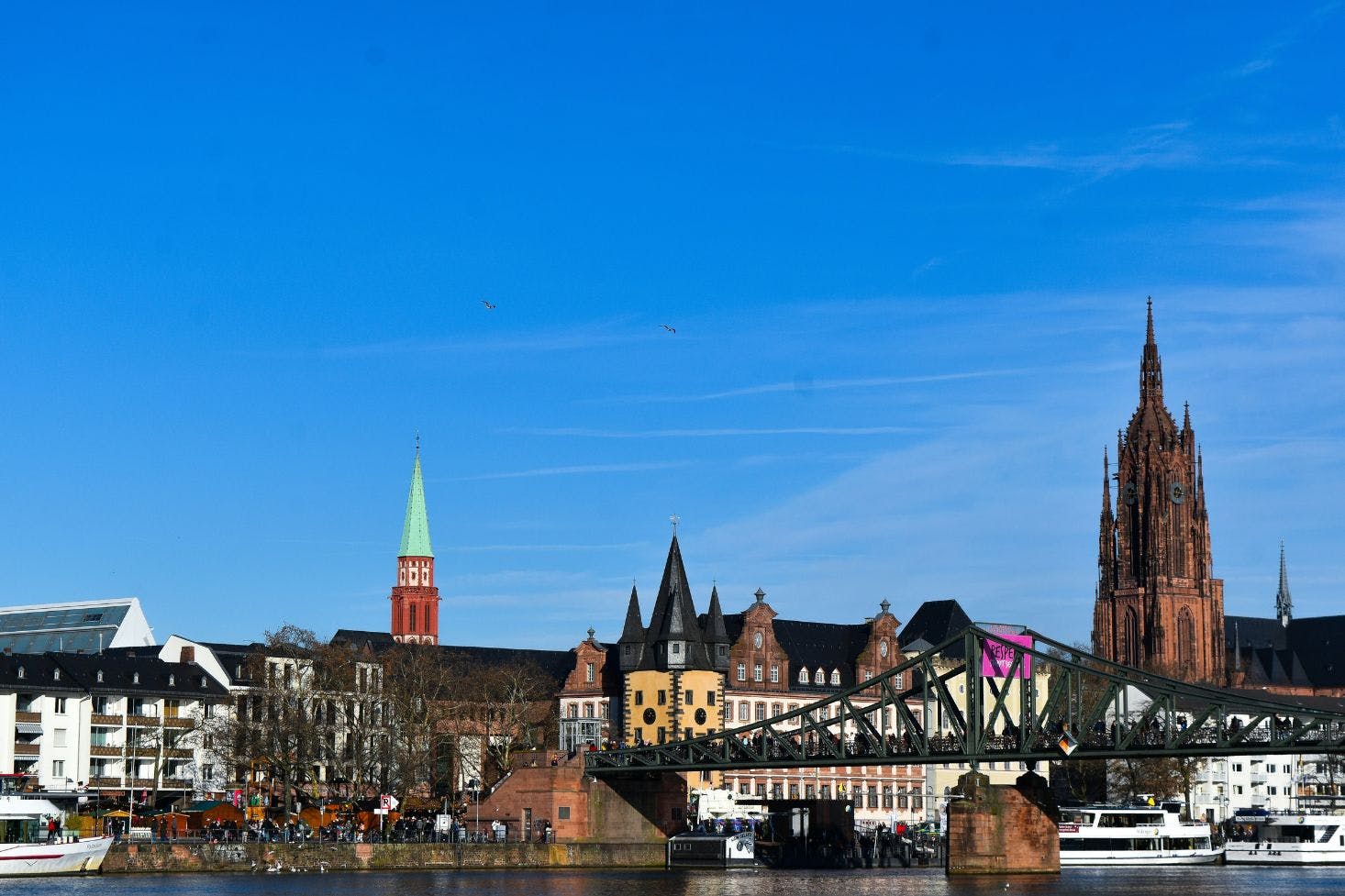 Frankfurt skyline featuring the historic Frankfurt Cathedral, colorful buildings, Eiserner Steg bridge, and a river view