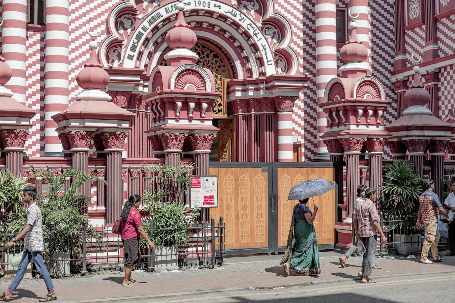 People walking by the ornate pink and white Jami Ul-Alfar Mosque in Colombo, Sri Lanka