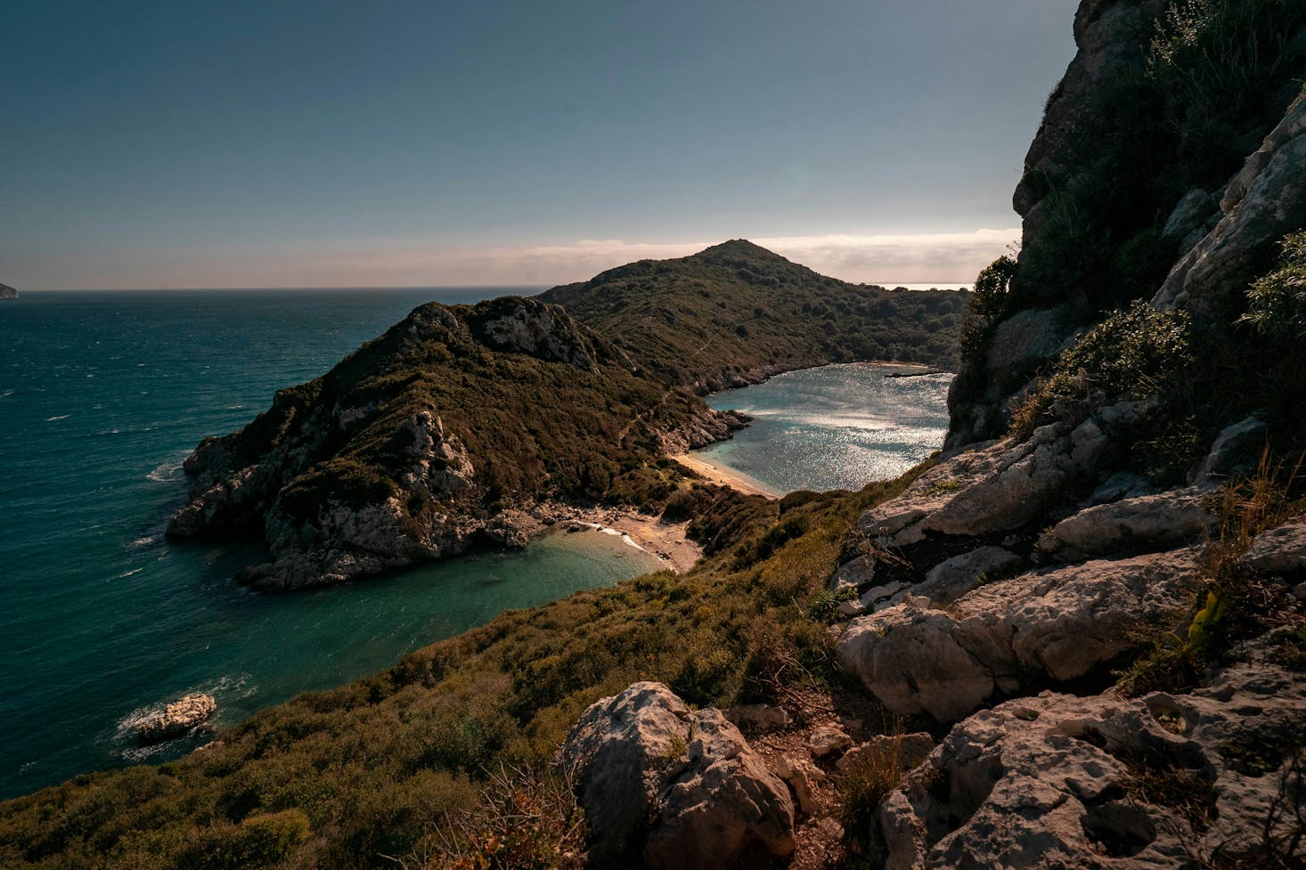 Spiagge adiacenti di Corfù viste dall'alto, con promontorio roccioso tutt'intorno e cielo sereno