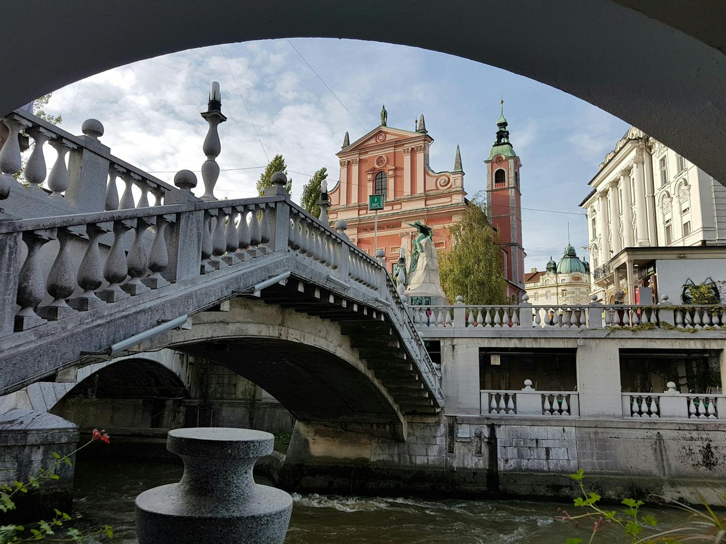 Ponte sul fiume Ljubljanica a Lubiana, con chiesa e altri edifici in secondo piano e cielo sereno sullo sfondo