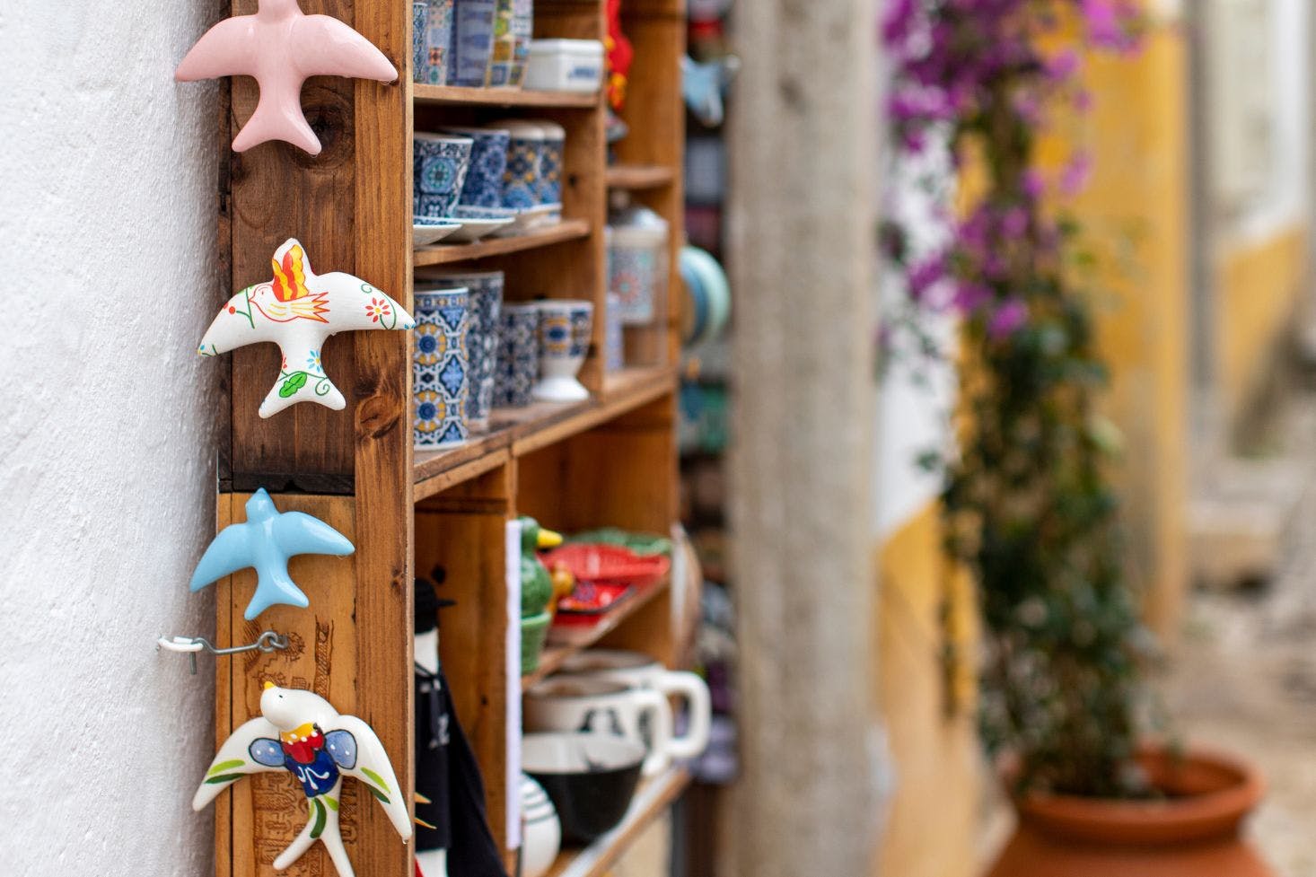 Colorful ceramic bird souvenirs and patterned cups, displayed on a shelf on the street