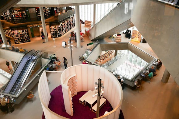 A shopping area in Oslo with modern architecture, bookshelves, escalators, seating, and people browsing and working