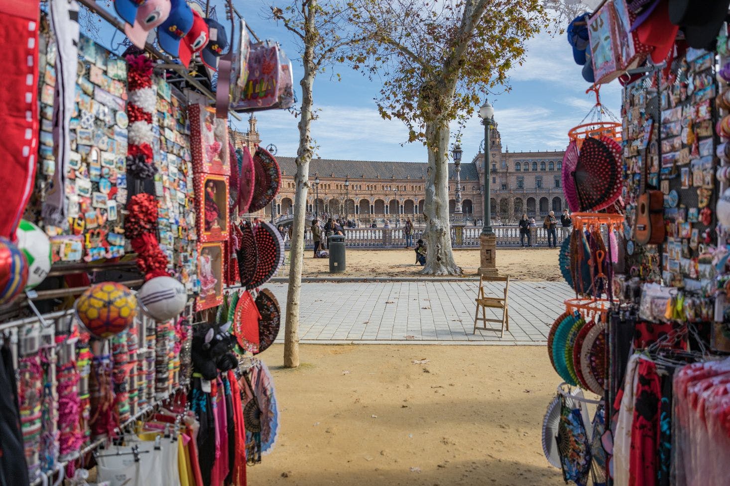 View of Plaza de España, Seville, from a street stall with colorful trinkets like bracelets, magnets, and scarves