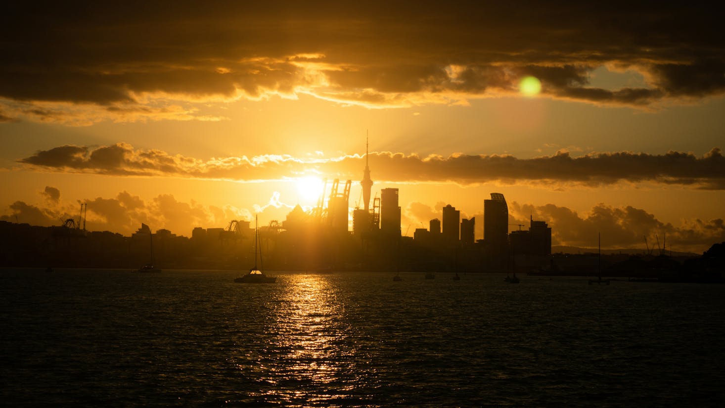 The silhouette of the Auckland skyline with an orange sunset