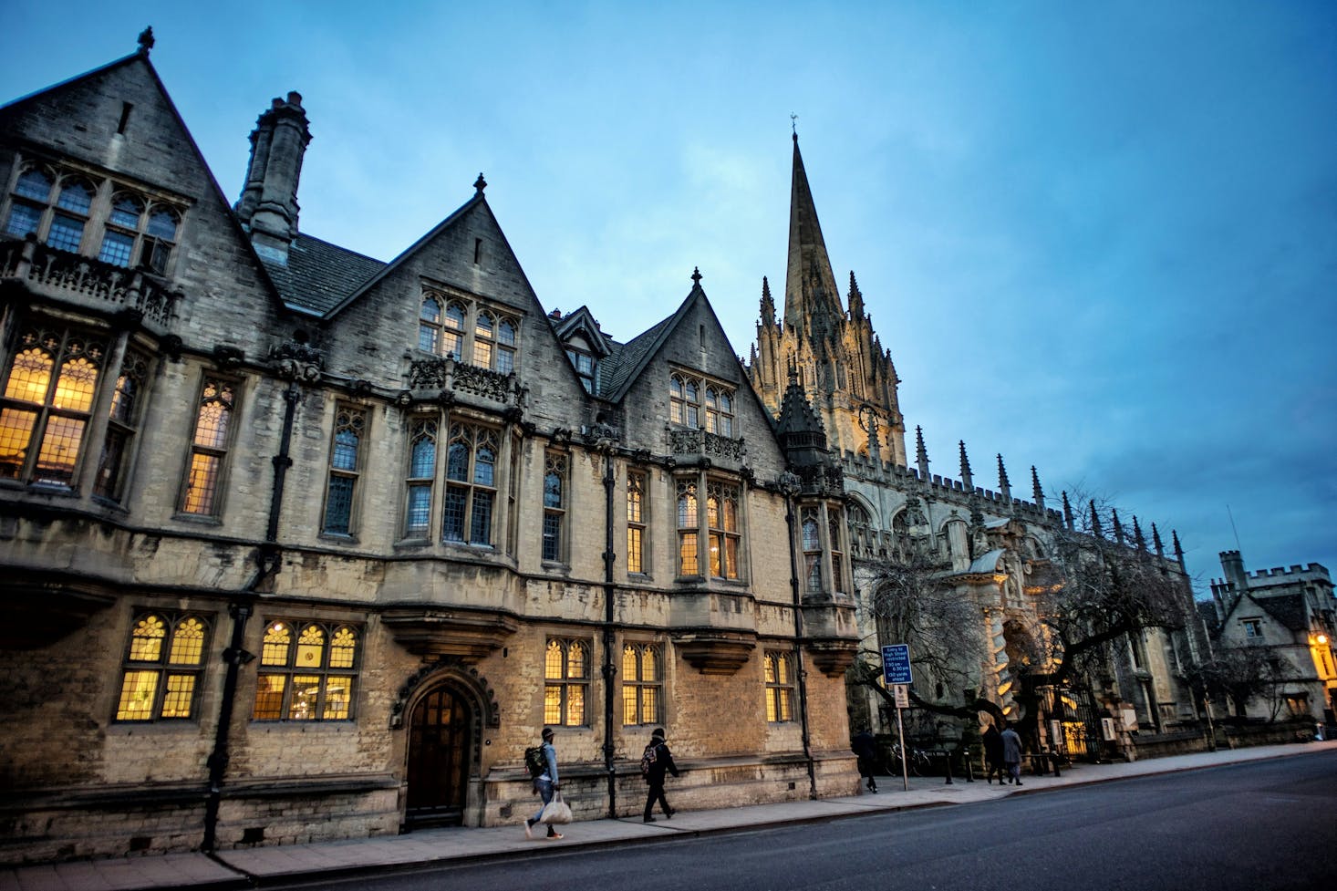 A gothic building in Oxford with people walking by at dusk