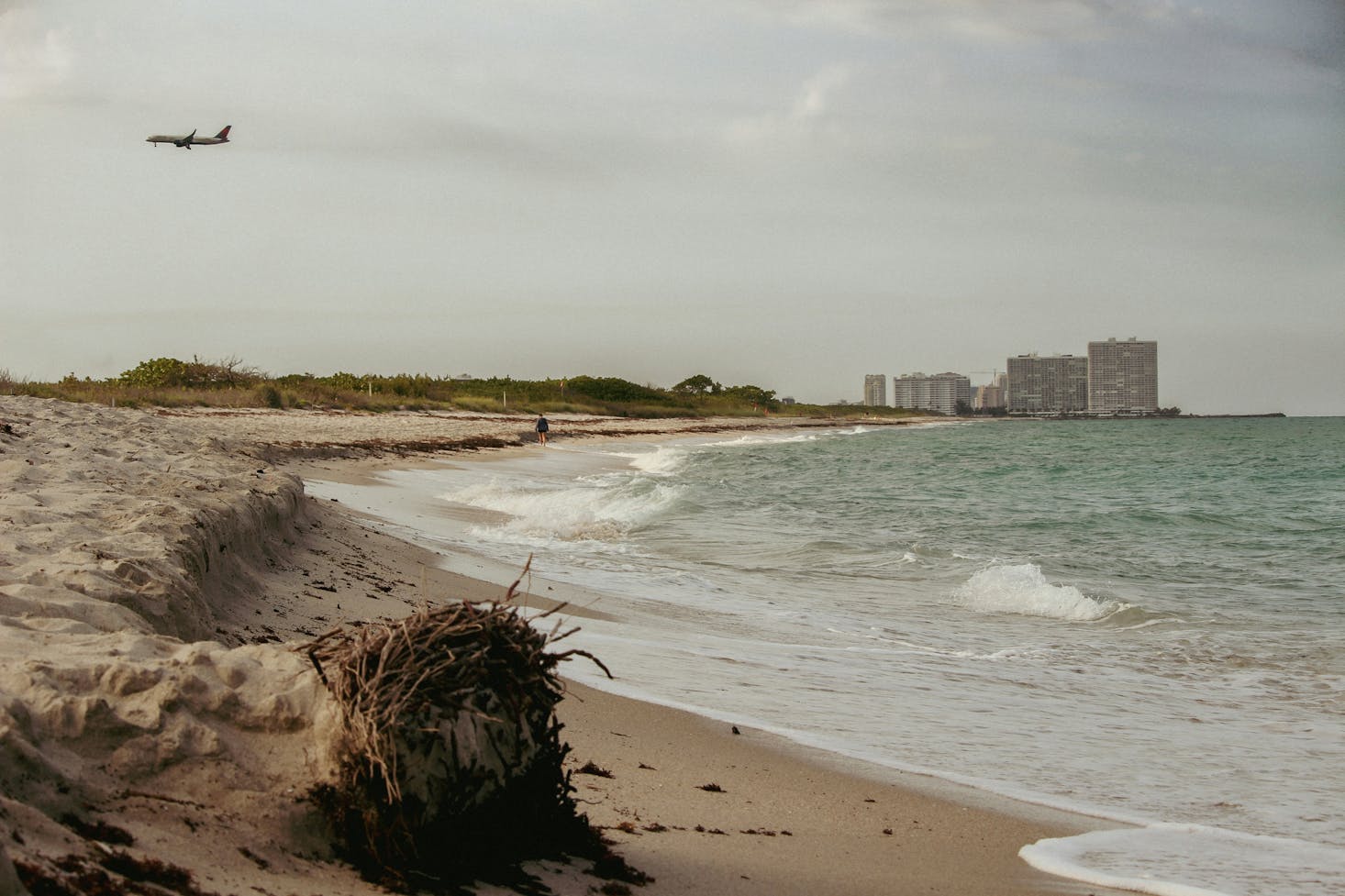 A deserted beach in Fort Lauderdale with the city in the distance and a plane overhead