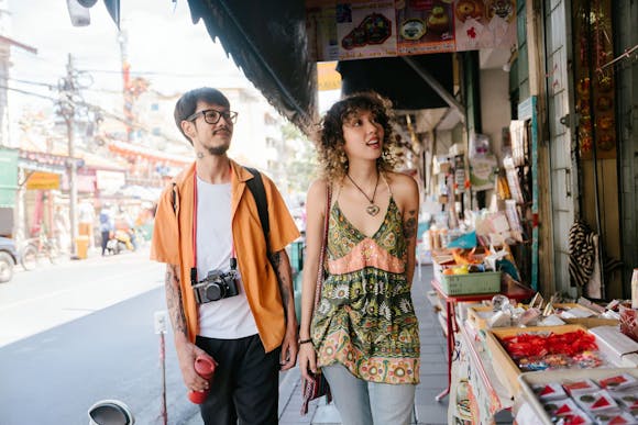 A black-haired young man and curly blonde woman looking around street stalls in Chinatown Bangkok