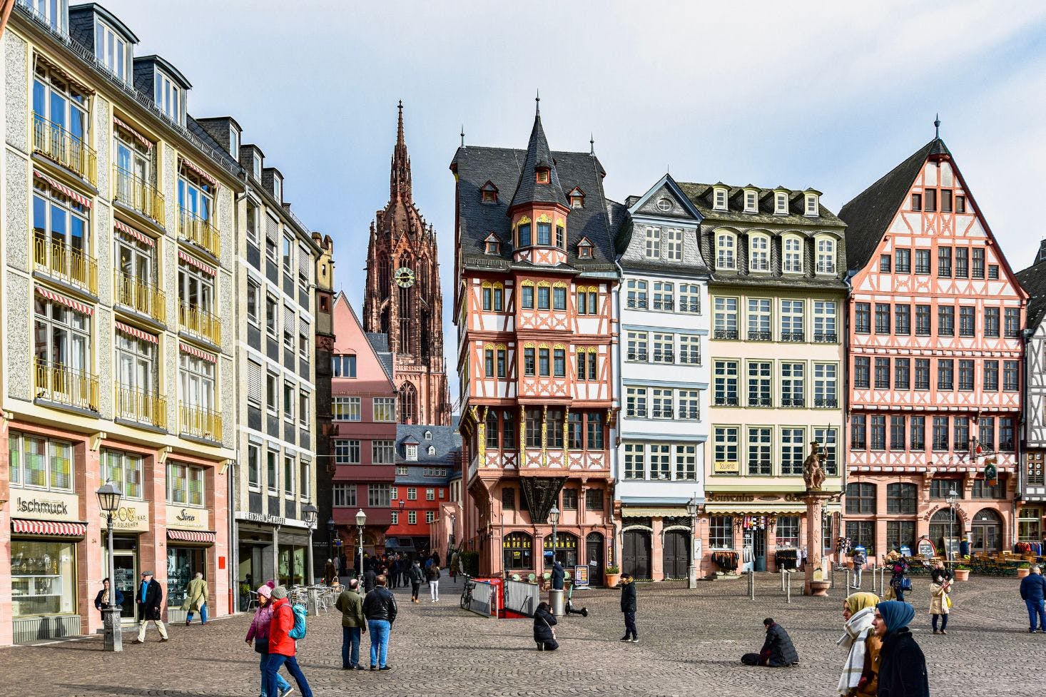 Busy Römerberg Square with locals walking by the shops and tourists taking photos in front of the Römer building