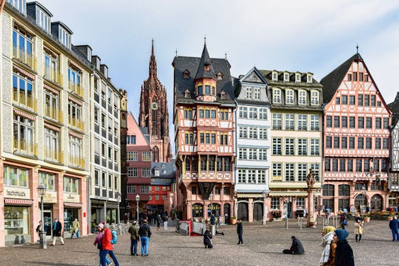 Busy Römerberg Square with locals walking by the shops and tourists taking photos in front of the Römer building