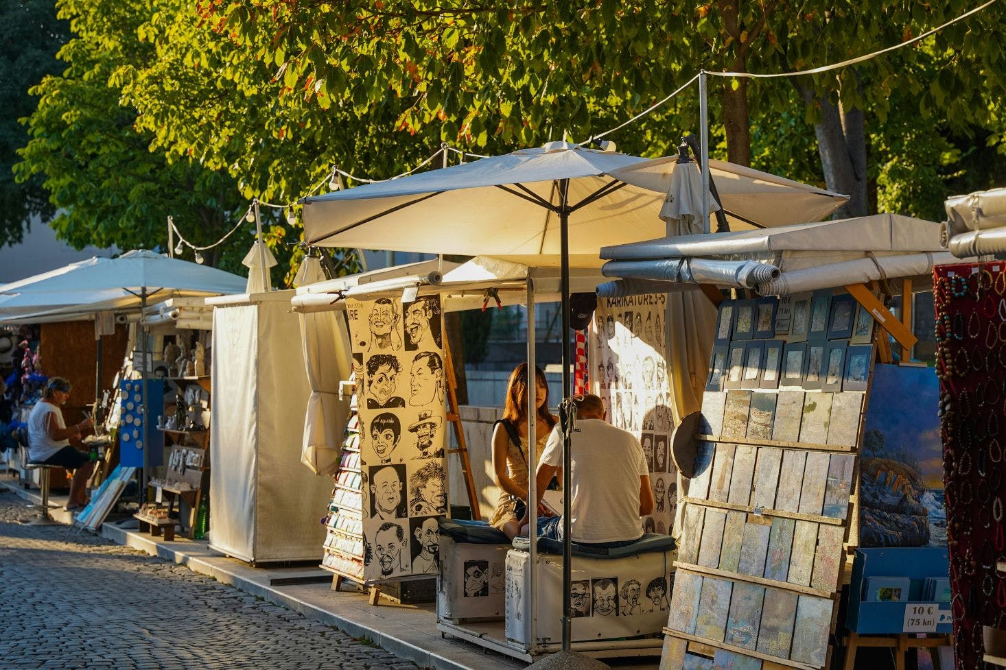 Street stalls in Split with an artist drawing a girl, surrounded by colorful caricatures and artwork for sale