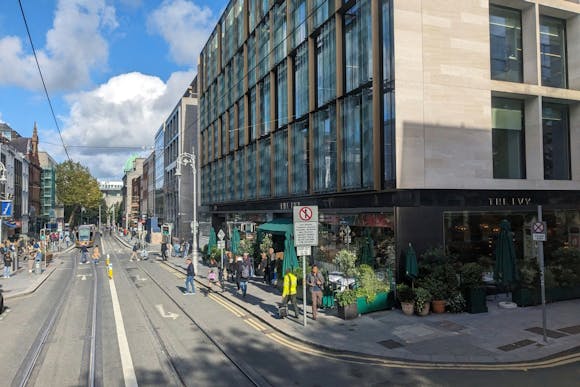 A street view of modern and historic buildings, a tram, people walking, and outdoor seating at The Ivy, Dublin