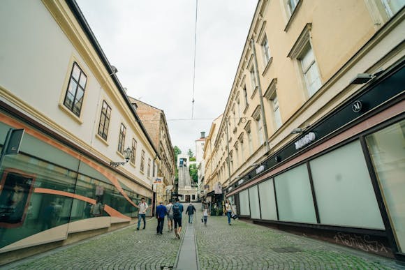 A cobbled shopping street in Zagreb with a view of the old funicular above