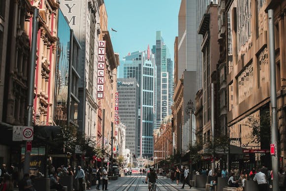 The busiest street, George Street in Sydney, lined with shops, cafes, locals sitting in cafes and a cyclist 