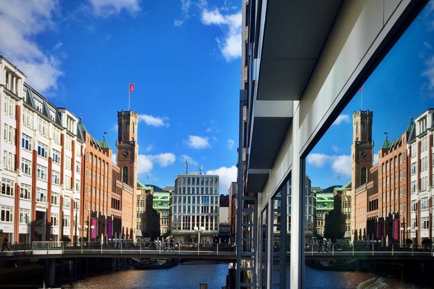 View of the Hamburg skyline with the Elbe River, a bridge, the Port Clock Tower, and nearby shops