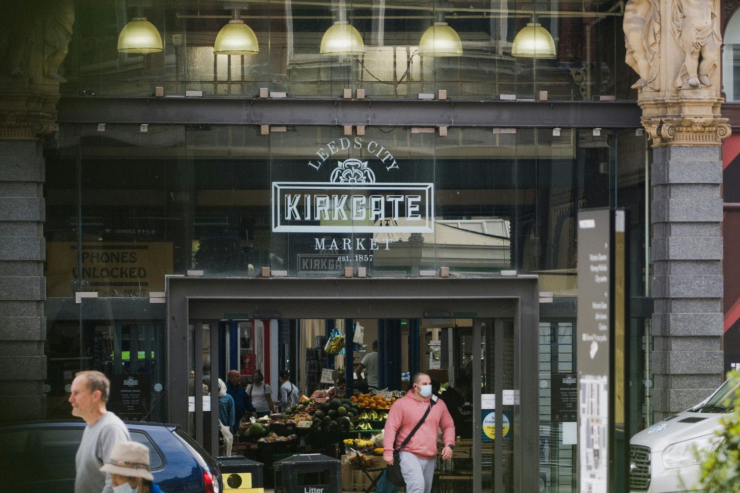 View of Kirk Gate Market’s glass entrance in Leeds with two men and a woman walking out of the market