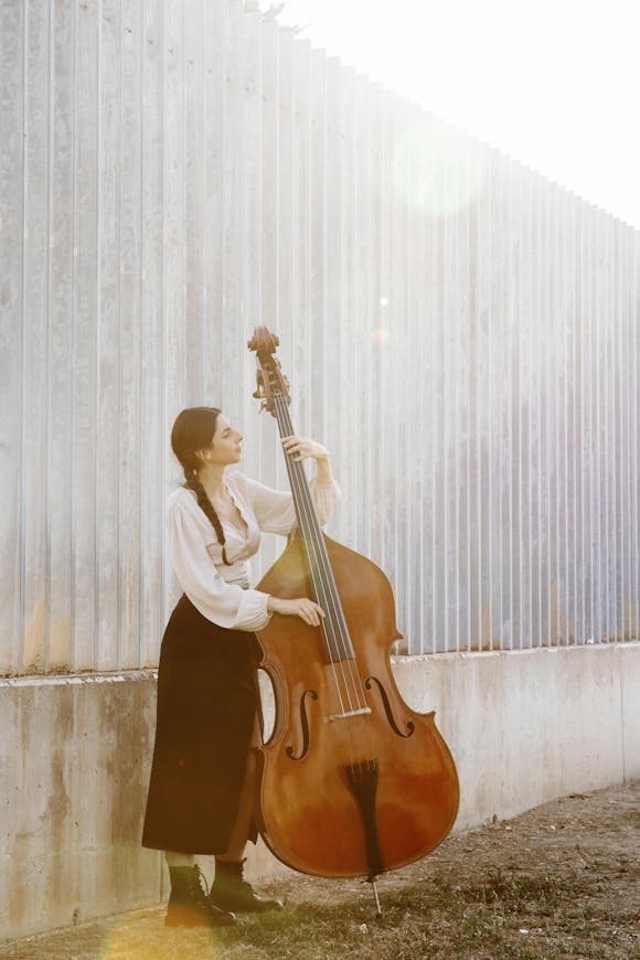 A woman playing a double bass outdoors with sunlight shining on her