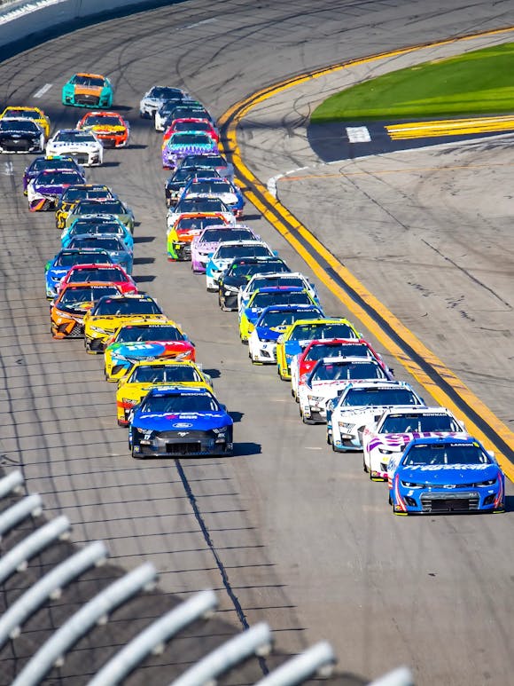 Vibrantly colored race cars speeding around the track during the Bluegreen Vacations Duel