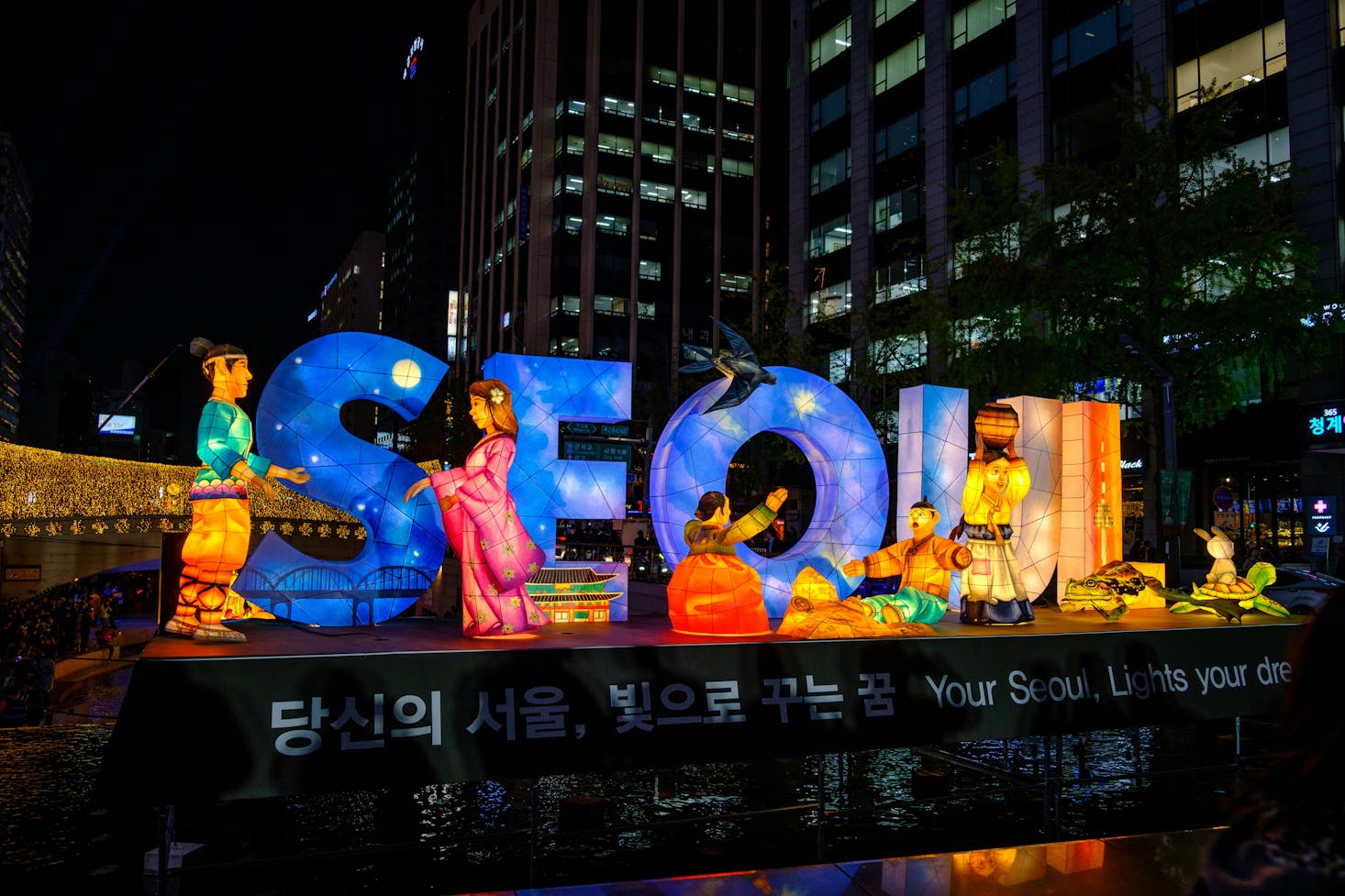 An illuminated sign for "SEOUL" in blues, reds, and yellow at night