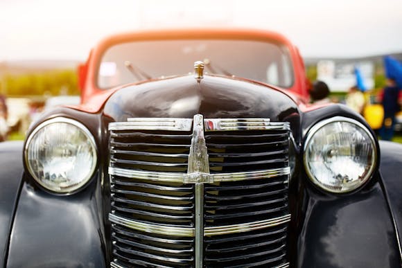 A close-up of a vintage car's front grille and headlights under warm sunlight