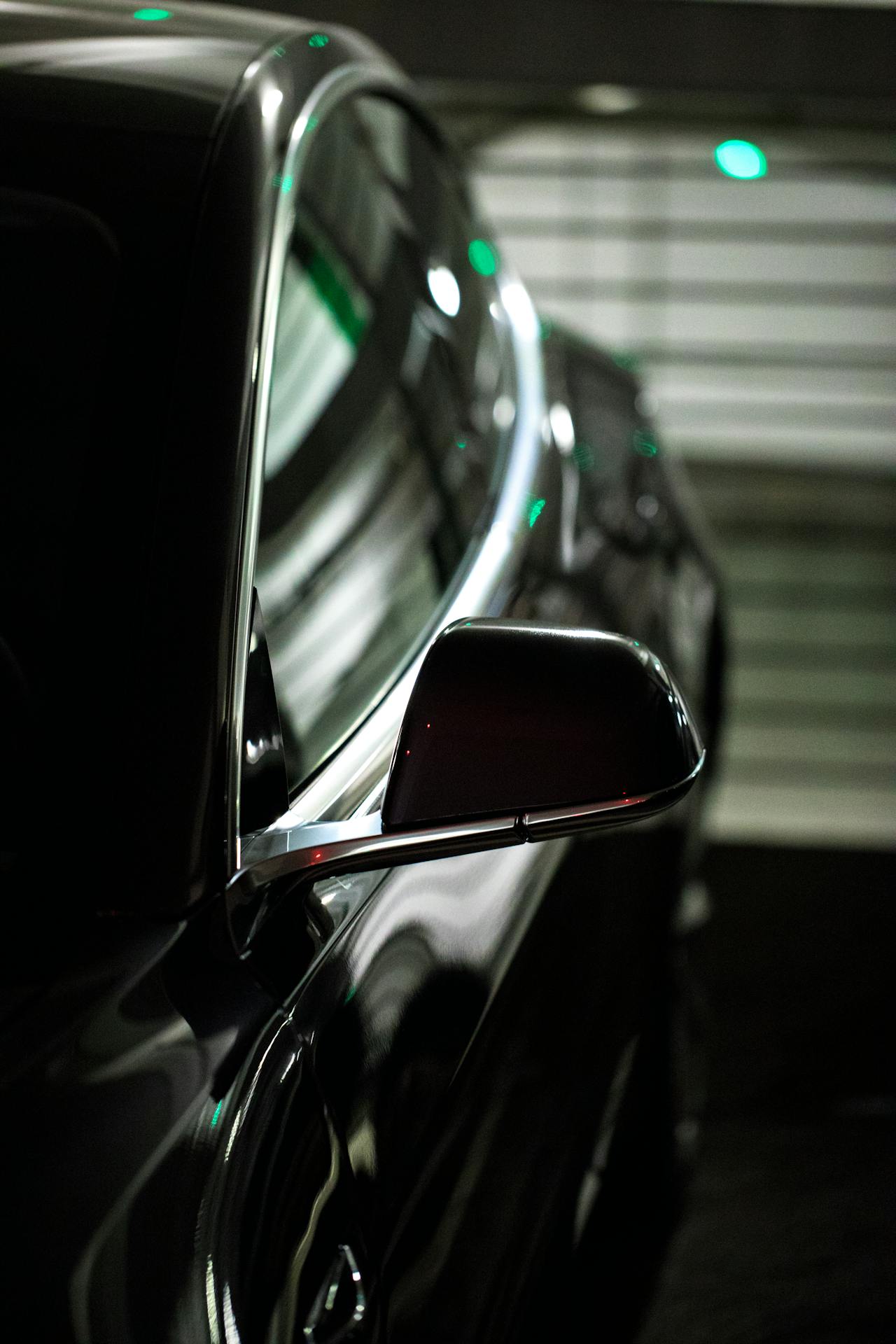 Close-up view of a sleek, dark-colored car in a dimly lit environment, emphasizing the car's glossy finish and modern design