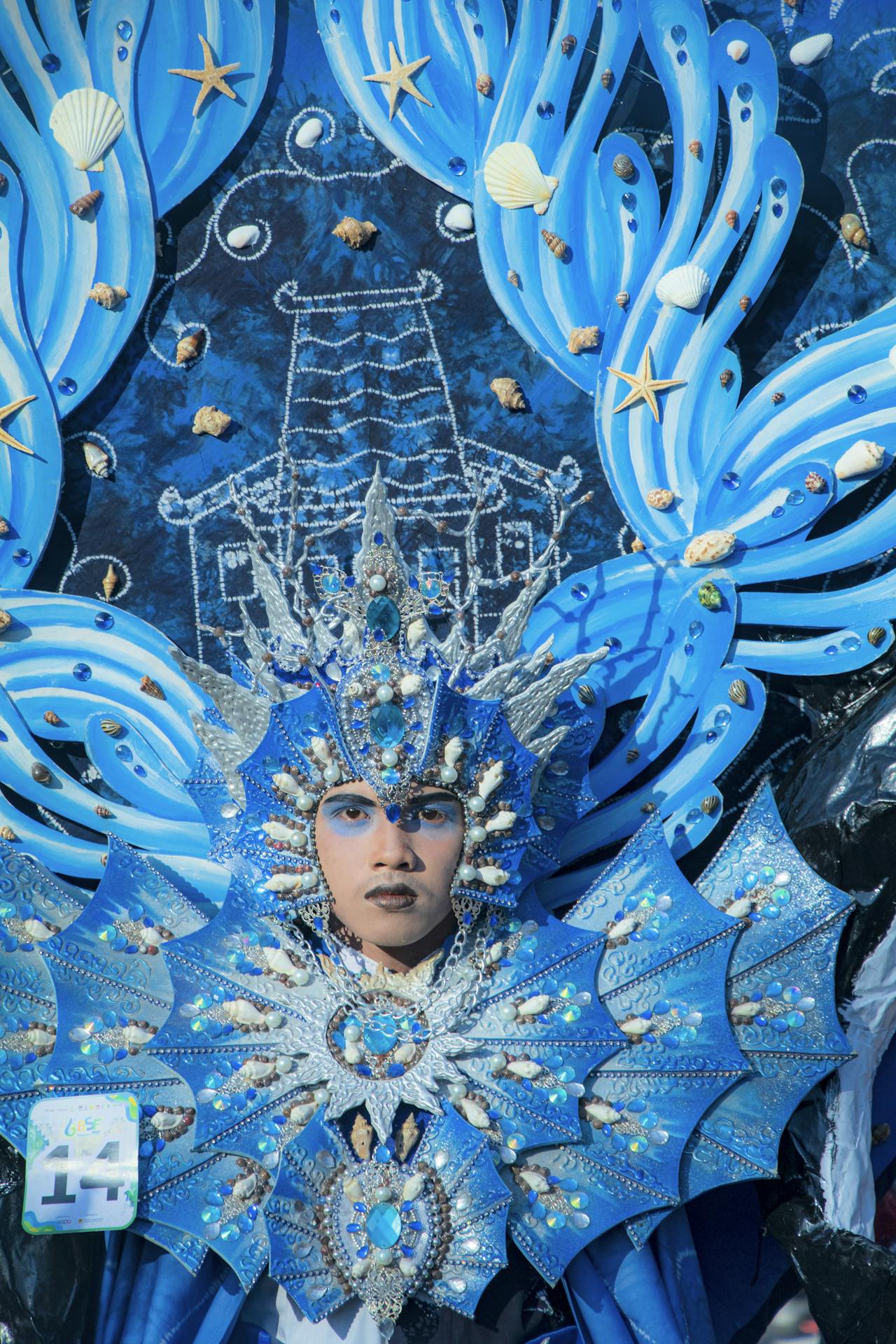 A person dressed in an elaborate blue and silver costume adorned with shells and sea-themed decorations during a carnival event