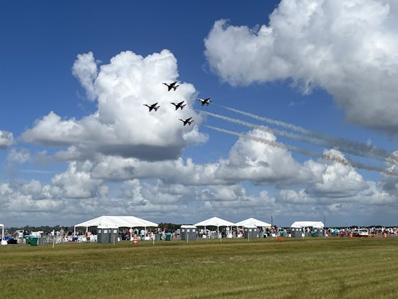 A formation of fighter jets performs an aerial display with smoke trails against a bright blue sky