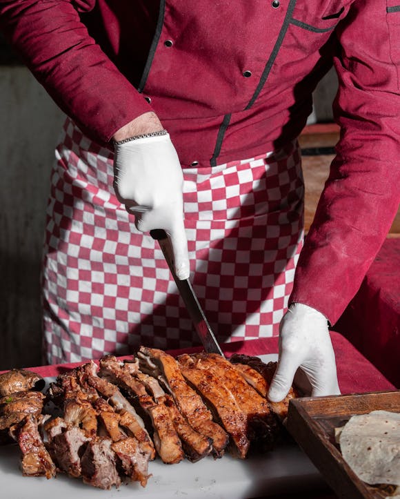 A chef in a red uniform slicing grilled meat on a cutting board