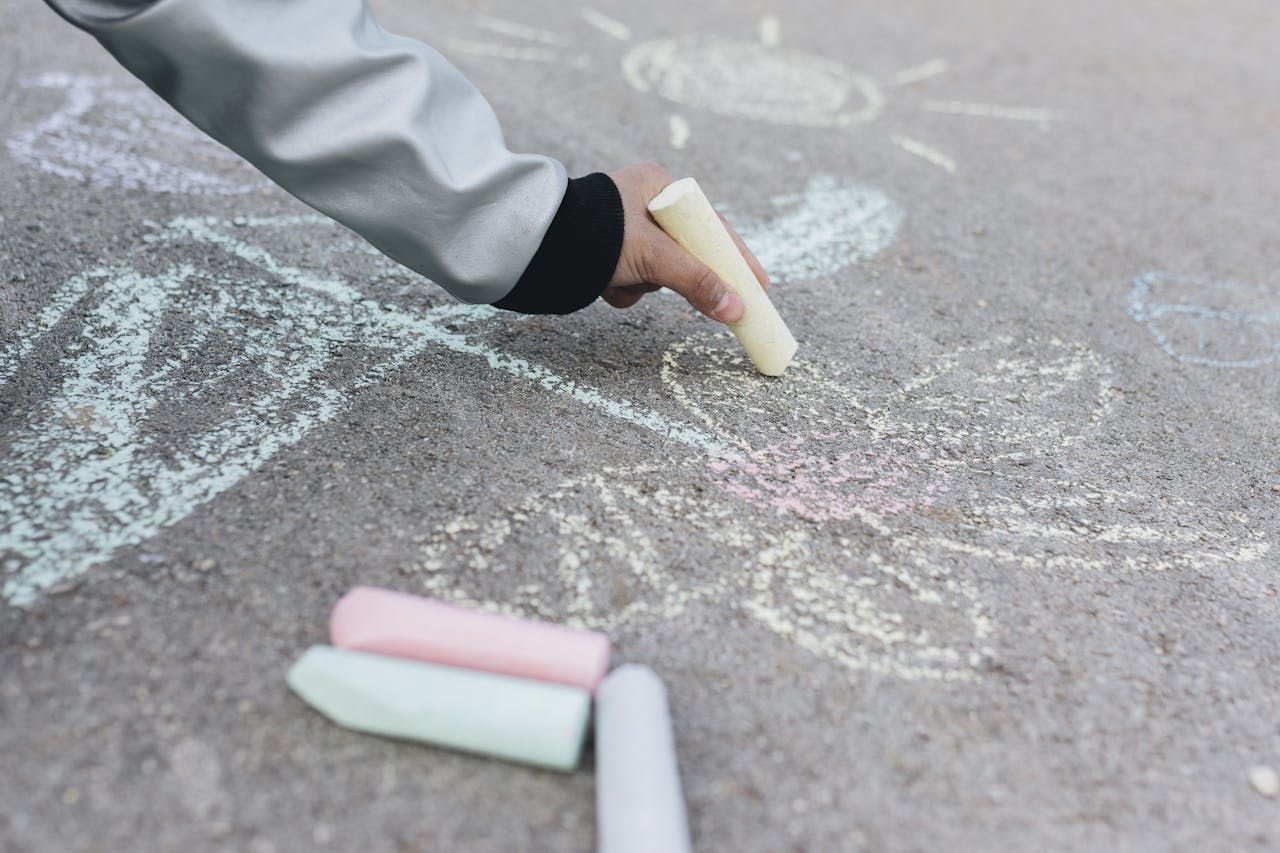 A close-up of a hand drawing colorful chalk art on pavement 