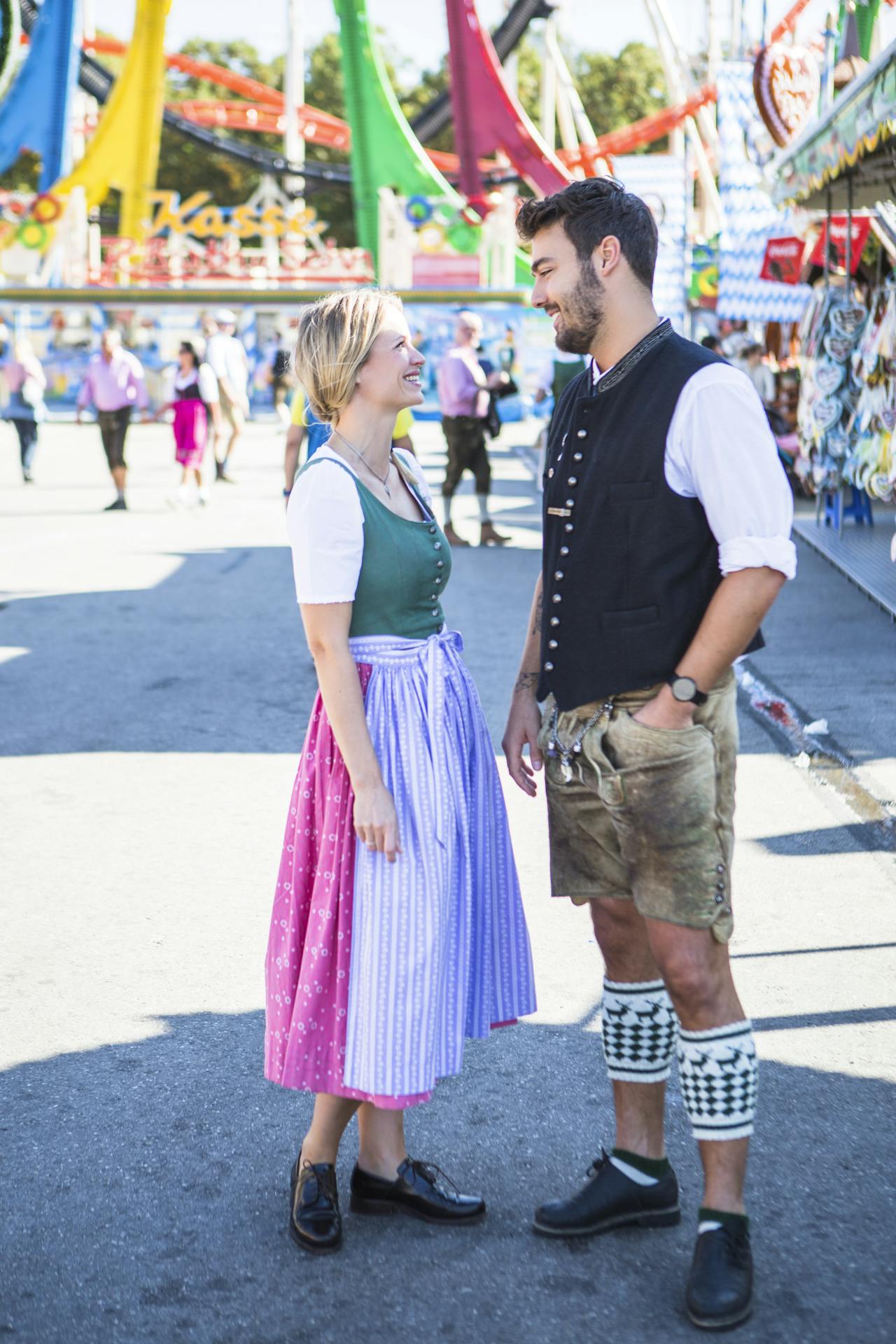 Smiling man and woman wearing dirndl and lederhosen standing on street at a fair in Munich